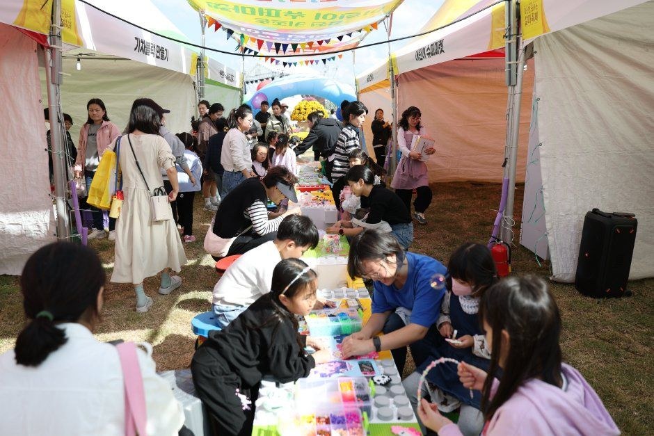 천막 아래에서 아이들과 보호자가 체험 재료를 들고 둘러앉은 축제 체험 부스