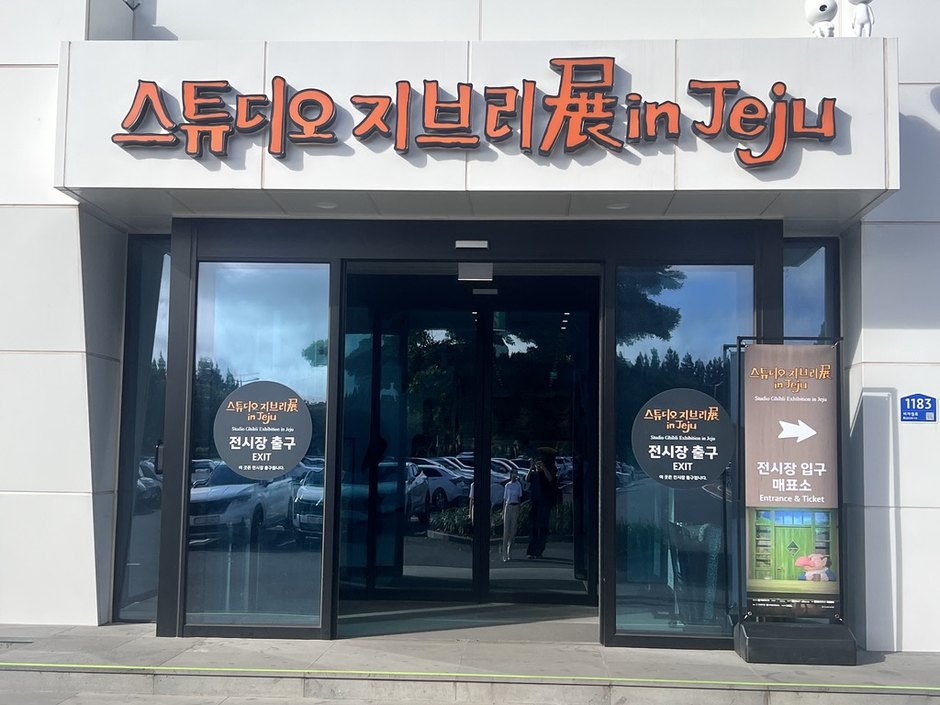 전시장 출구라고 적힌 유리문 옆에 입구 매표소를 가리키는 화살표 입간판이 서 있는 건물 정면