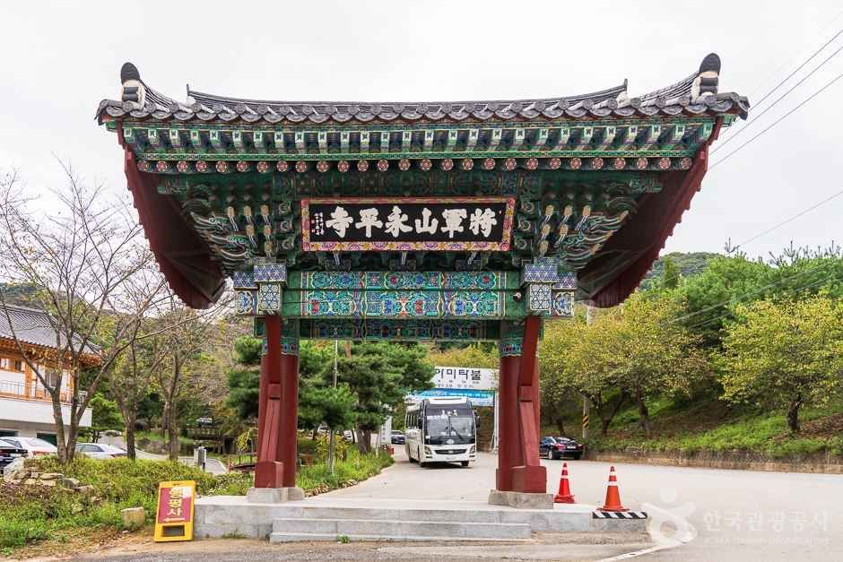 단청으로 화려하게 장식된 영평사 일주문, 뒤로 산길과 버스 한 대가 지나는 모습