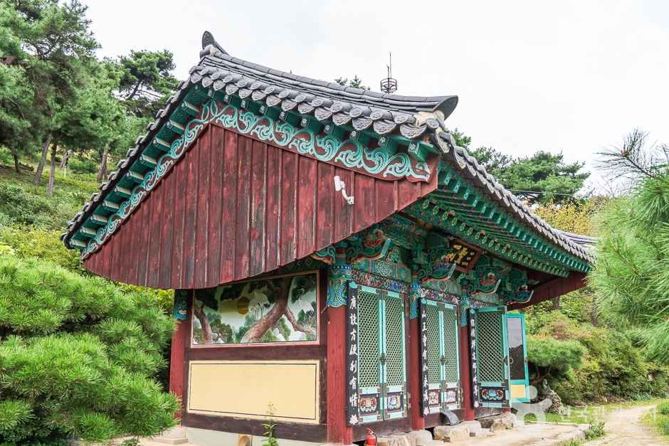 소나무 숲에 둘러싸인 영평사 전각, 처마 아래 단청과 벽화가 화려하게 장식된 모습