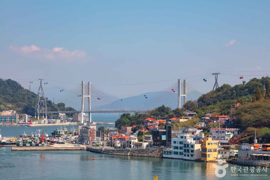 푸른 하늘 아래 돌산대교와 케이블카, 여수 항구의 건물들이 보이는 풍경